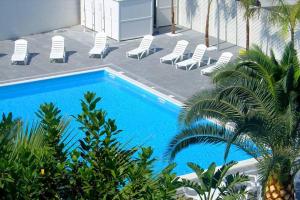 a blue swimming pool with chairs and palm trees at Hotel La Terrazza in Barletta