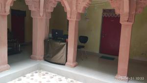 um quarto com colunas cor-de-rosa e uma mesa com um computador em Radha Krishna Home em Varanasi
