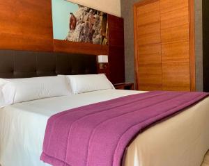 a bedroom with a large bed with a purple blanket on it at Hotel Balneario Valle del Jerte in Valdastillas