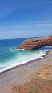 a beach with a rock formation in the ocean at HOTEL BEACH CLUB LEGZIRA in Sidi Ifni