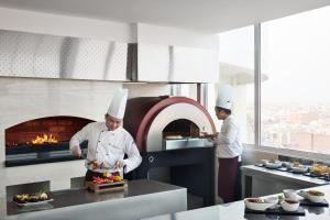 2 chefs que preparan comida en una cocina con horno en Mövenpick Hotel Qassim, en Buraidah