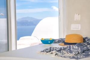 a hat and a bowl on a table in front of a window at White Cave House in Oia
