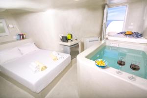 a room with a bed and a tub with glasses of wine at White Cave House in Oia