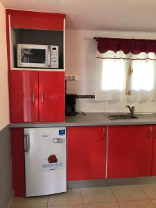 una pequeña cocina con armarios rojos y nevera blanca. en La tourterelle de Neron, en Le Moule