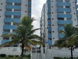 a tall apartment building with palm trees in front of it at Apto Verde Água in Mongaguá