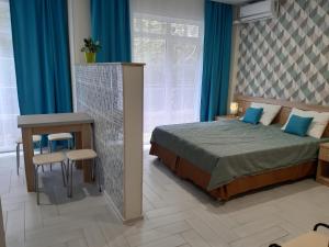 a bedroom with a bed and a table and blue curtains at Apartments Tsaritsino in Adler