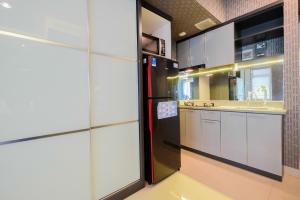 a kitchen with a black refrigerator and white cabinets at Fabulous Studio Grand Kamala Lagoon Apartment By Travelio in Pulosirih