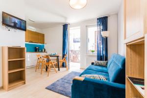 a living room with a blue couch and a kitchen at Apartamenty NCNK Leśny Zaułek Sztutowo in Sztutowo