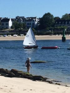 a person standing on the beach with a sail boat at Les jardins du vivier in Combrit