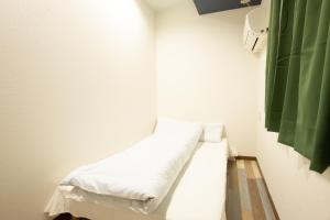大阪市にある123 ゲストハウスの白いシーツと緑のカーテンが備わるベッド1台が備わる客室です。