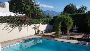 a swimming pool in front of a white wall with flowers at Franschhoek Village House in Franschhoek