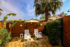 a patio with three white chairs and a brick wall at Aggeliki's Hideaway Studio in Lefkada
