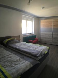 ein Schlafzimmer mit einem Bett, einem Fenster und einem roten Stuhl in der Unterkunft Ferienwohnung Alte B3 in Ringsheim