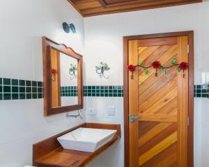 baño con lavabo, espejo y puerta en Suítes Yamamoto Ilhabela, en Ilhabela
