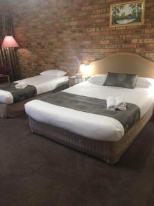two beds in a room with a brick wall at Pines Country Club Motor Inn in Shepparton