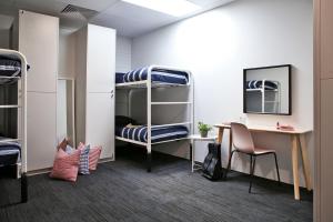 a dorm room with bunk beds and a desk and a table at Spinners Hostel in Perth