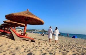 2 personnes marchant sur une plage avec un parasol dans l'établissement Barry Boutique Hotel Sanya, à Sanya