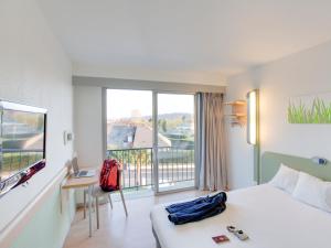 a hotel room with a bed and a desk and a window at ibis budget Pau Lescar in Lescar