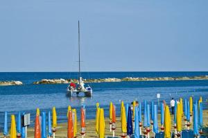 ein Boot im Wasser in der Nähe eines Strandes mit bunten Sonnenschirmen in der Unterkunft Hotel Plaza in Pesaro