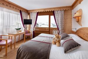 un osito de peluche sentado en una cama en un dormitorio en Chalet-Hôtel Neige et Roc, The Originals Relais (Hotel-Chalet de Tradition), en Samoëns