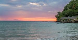 um pôr do sol sobre a água com uma casa na costa em L'heure Bleue em Ambatoloaka