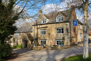 um velho edifício de pedra com um banco em frente em The Crown Inn, Church Enstone em Chipping Norton