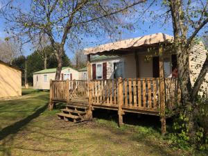 a small house with a wooden porch next to a tree at Camping Arquebuse in Auxonne