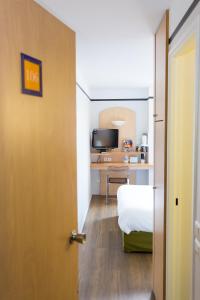 a room with a bed and a desk with a television at Hotel inn Grenoble Eybens Parc des Expositions Ex Kyriad in Eybens