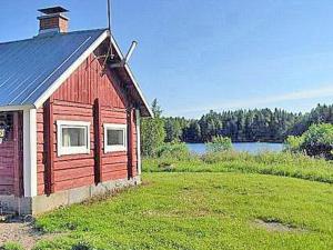a red building with a grass yard next to a lake at Holiday Home Pikku-villa by Interhome in Vähäsalmi