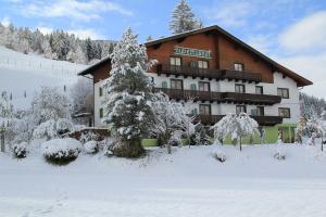 ein großes Gebäude im Schnee mit einem Baum in der Unterkunft Pension Hubertushof beim Römerbad in Bad Kleinkirchheim