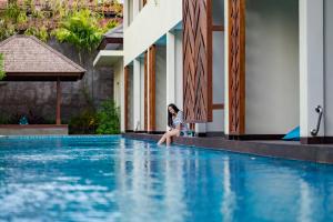 a woman sitting on the edge of a swimming pool at Anja Jimbaran in Jimbaran