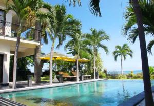 a swimming pool in front of a building with palm trees at Villa Dunia Impian in Kubutambahan