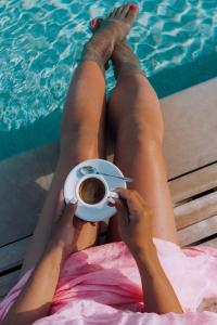 una mujer tendida frente a una piscina sosteniendo una taza de café en Masseria Palane en Patù