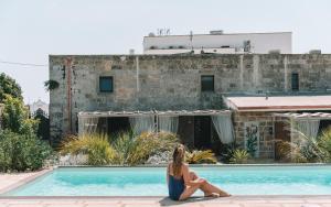 una mujer sentada en el borde de una piscina en Masseria Palane en Patù