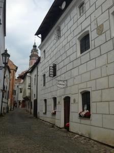 an alley with a white building with a clock tower at Penzion Dům u barvíře in Český Krumlov