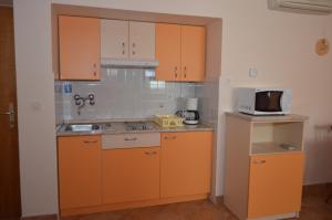 eine Küche mit orangefarbenen Schränken und einer Mikrowelle in der Unterkunft Apartments Anci in Mali Lošinj
