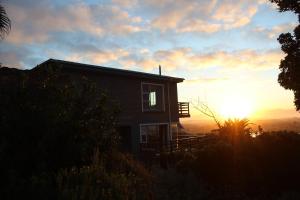 a house on a hill with the sunset in the background at Bluebottle Guesthouse in Muizenberg