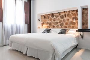 a bedroom with a large white bed with a stone wall at Can Vent Boutique Hotel in Alcudia