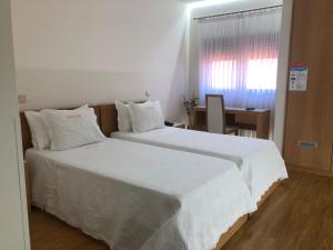 a bedroom with a large bed with white sheets and a window at Hotel Aeroporto in Maia