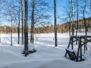 a snow covered park with two benches and trees at Holiday Home 2234 by Interhome in Savonranta