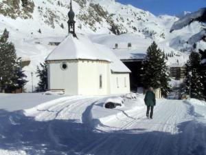 a person walking down a snow covered road next to a church at Apartment Almenrausch Parterre by Interhome in Riederalp