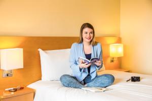 a woman sitting on a bed reading a book at ibis Deira Creekside Dubai in Dubai