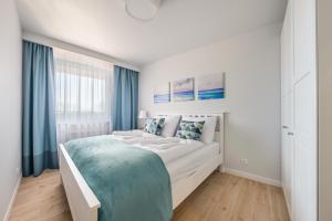 a white bedroom with a large bed with blue curtains at Wyspa Solna, Sun & Snow in Kołobrzeg