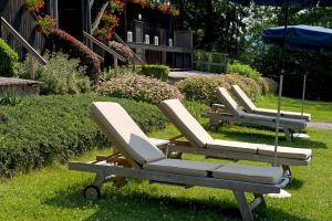 three lounge chairs and an umbrella in the grass at Inselhotel Faakersee in Faak am See