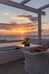 a sunset on the beach with a table and chairs at Magic View Suites Mykonos in Mikonos