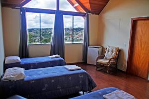 une chambre avec deux lits et une chaise et une fenêtre dans l'établissement Pousada AlpenRose, à Campos do Jordão