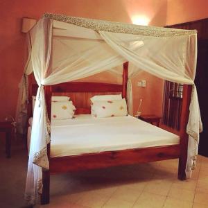a bedroom with a canopy bed with white sheets and pillows at Ghepard Eden in Watamu
