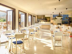 a restaurant with white tables and chairs and a kitchen at Hapimag Resort Cefalù in Cefalù