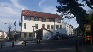 un grand bâtiment blanc avec des voitures garées devant lui dans l'établissement Zorn Hotel Duinlust, à Noordwijk aan Zee