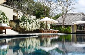 a pool with umbrellas and chairs next to a house at REVĪVŌ Wellness Resort Nusa Dua Bali in Nusa Dua